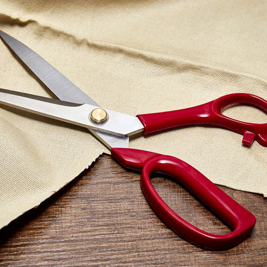 Red-handled scissors on a wooden surface with beige fabric