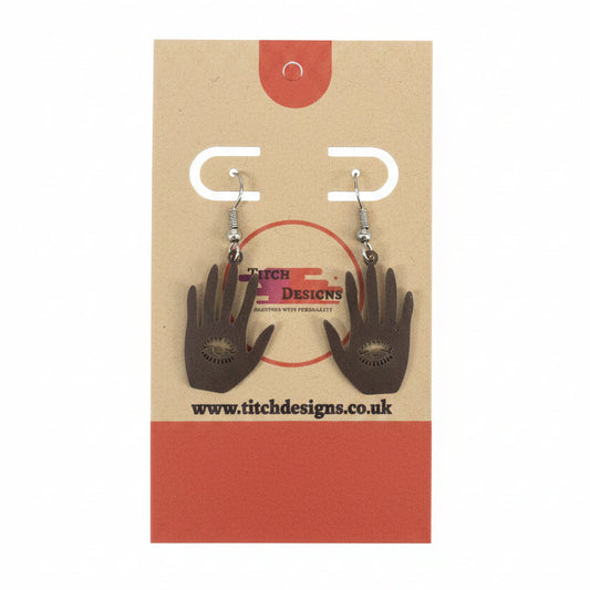 A pair of hand-shaped dangle earrings with silver fishhook wires, displayed on a brown paper backing card with red accents.