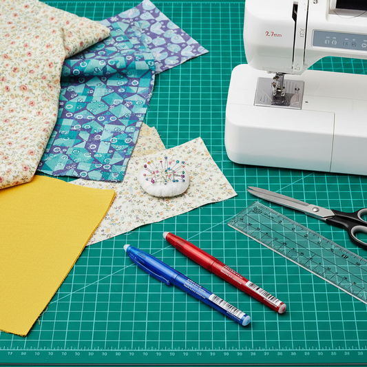 Sewing machine on a green cutting mat with fabric, scissors, and measuring tools.