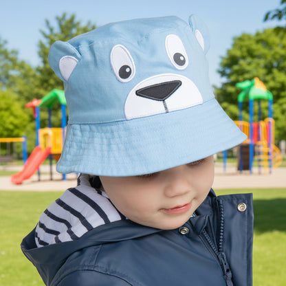 Child wearing a blue bear-themed hat with a park in the background 