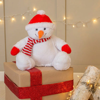 Plush snowman toy on a gift box with festive lights in the background