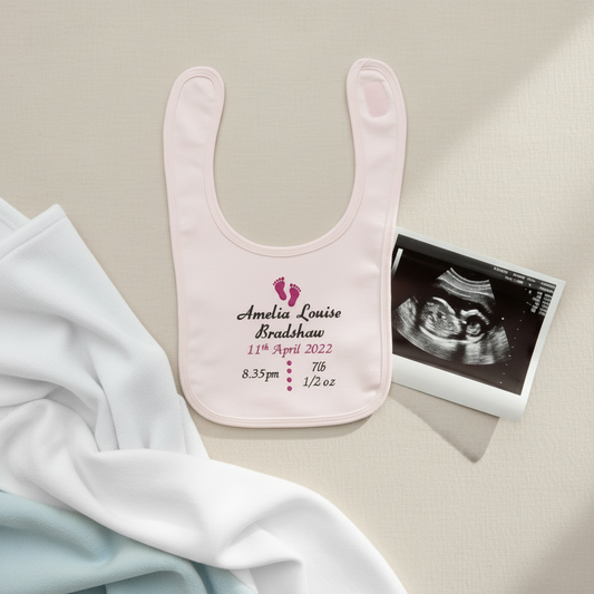 Pink baby bib with personalized text and ultrasound photo on a beige surface