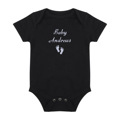 A black short-sleeve baby bodysuit with 'Baby Andrews' and baby footprints embroidered in white on the chest, displayed on a solid white background.