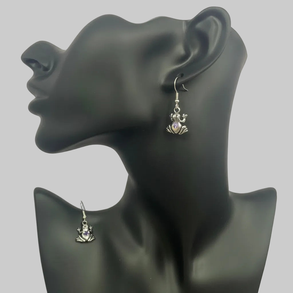 A pair of silver-toned dangle earrings displayed on a matte black female mannequin bust, with one earring hanging from the ear and the other shown on the neck.