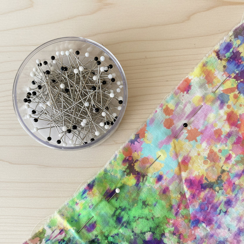Colorful fabric with pins and a container of pins on a wooden surface