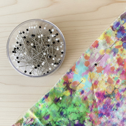 Colorful fabric with pins and a container of pins on a wooden surface