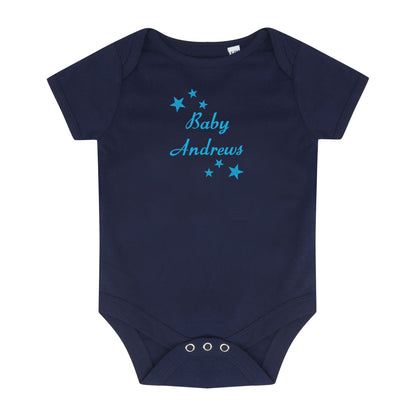 A navy blue short-sleeve baby bodysuit with 'Baby Andrews'embroidered in light blue script across the chest, surrounded by small light blue stars. The bodysuit has three silver metal snap closures at the crotch and is displayed flat against a solid white background.