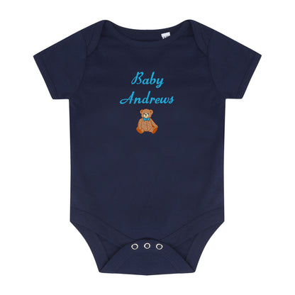 A navy blue baby short-sleeve bodysuit with 'Baby Andrews' embroidered in light blue script and a small brown teddy bear graphic on the chest, shown on a plain white background.