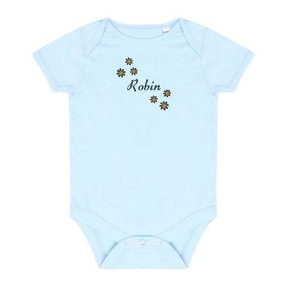 A light blue baby bodysuit with short sleeves and snap closures at the crotch, featuring the name 'Robin' in black script between small yellow and blue daisy graphics on the chest, displayed on a solid white background.