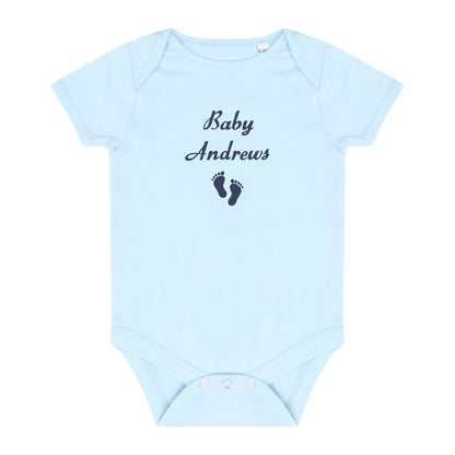 A light blue short-sleeve baby bodysuit with 'Baby Andrews' and a pair of dark blue baby feet embroidered on the chest, displayed flat against a white background.
