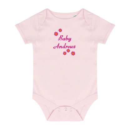 A light pink short-sleeve baby bodysuit with 'Baby Andrews' embroidered in pink script on the chest, surrounded by small pink and red flowers, shown on a plain white background.