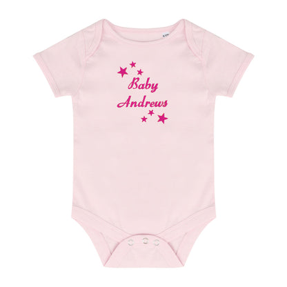 A light pink short-sleeve baby bodysuit with 'Baby Andrews' embroidered in dark pink script across the chest, surrounded by small pink stars, shown on a plain white background.
