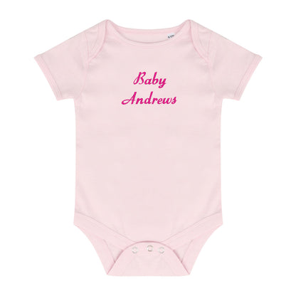 A light pink short-sleeve baby bodysuit with 'Baby Andrews' embroidered in pink script across the chest, displayed on a solid white background.