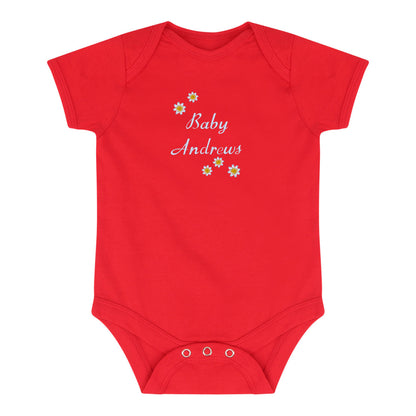 A red short-sleeve baby bodysuit with 'Baby Andrews' written in white script on the chest, decorated with small yellow and white flowers, and featuring three snap closures at the crotch.