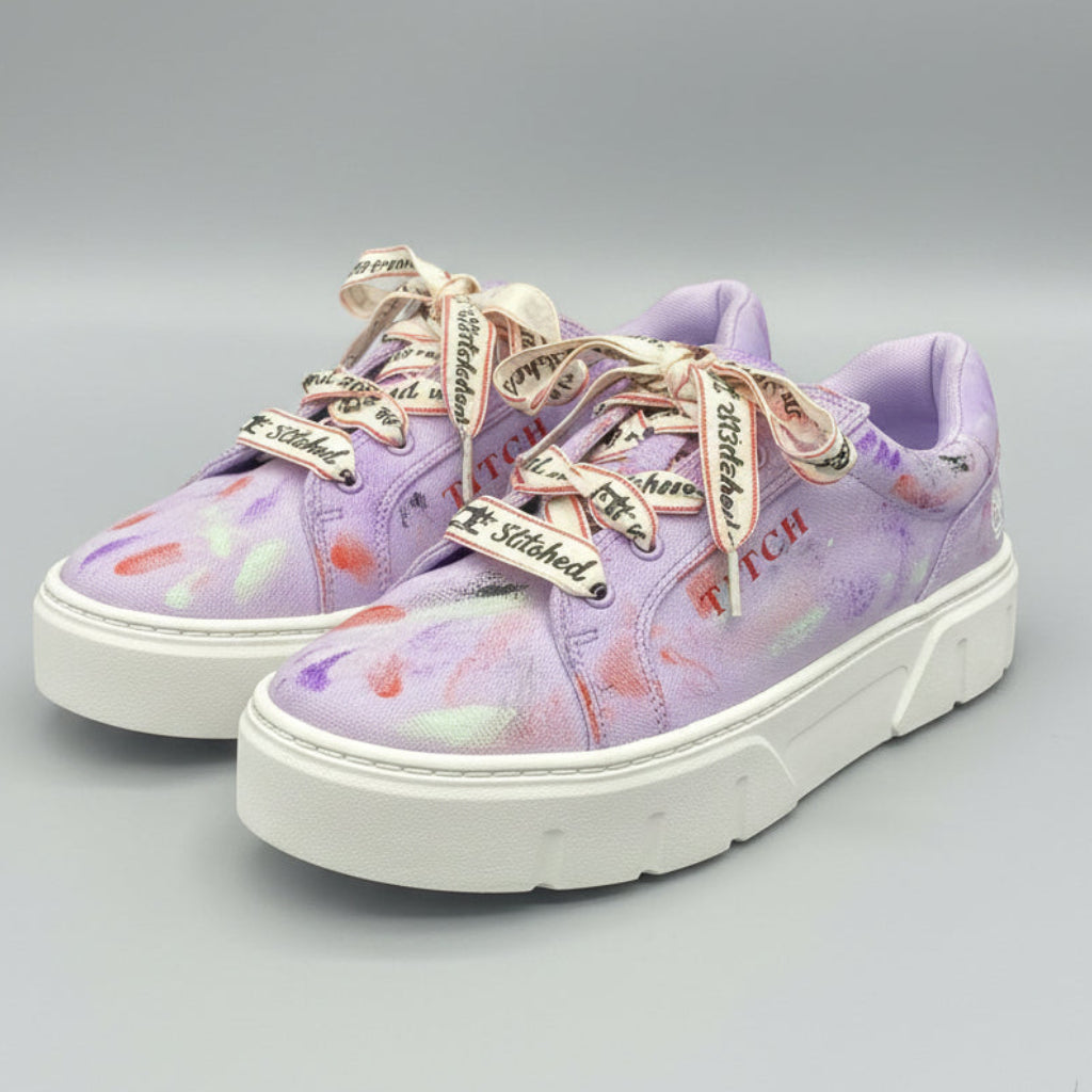 A pair of low-top platform sneakers in a light purple/lavender colorway with a colorful paint splatter pattern, featuring white soles and decorative silver and red laces. The brand name 'TITCH' is printed on the side of the shoes.