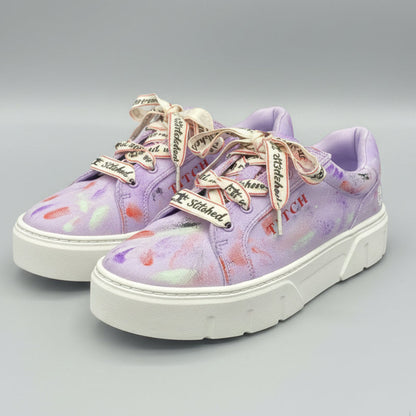 A pair of low-top platform sneakers in a light purple/lavender colorway with a colorful paint splatter pattern, featuring white soles and decorative silver and red laces. The brand name 'TITCH' is printed on the side of the shoes.