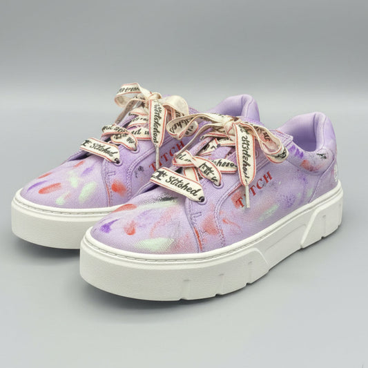 A pair of low-top platform sneakers in a light purple/lavender colorway with a colorful paint splatter pattern, featuring white soles and decorative silver and red laces. The brand name 'TITCH' is printed on the side of the shoes.