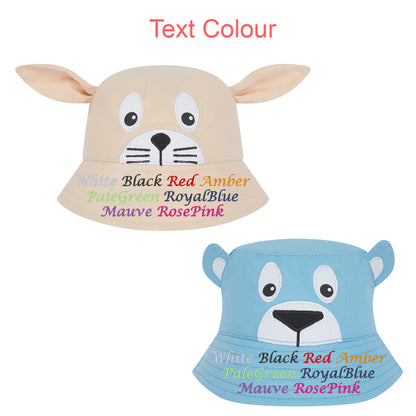 Two plush animal-face bucket hats on a white background, with the top hat beige/tan and the bottom hat light blue. Red text at the top reads 'Text Colour.
