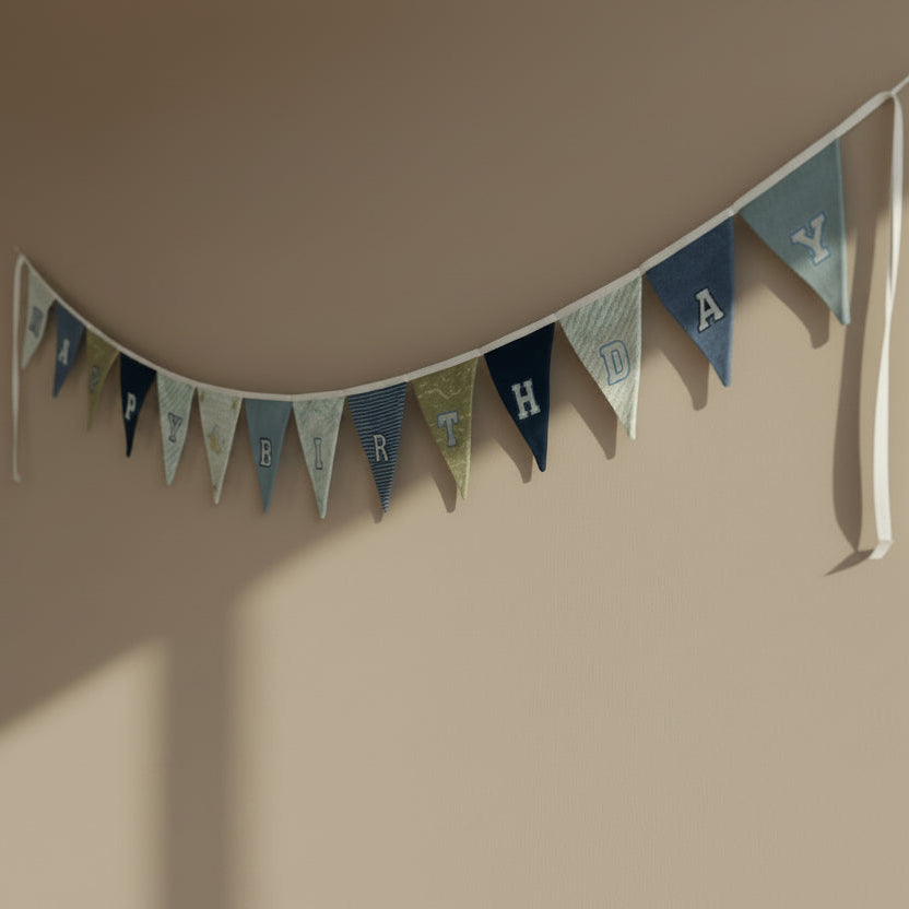 Handmade Birthday banner with blue and green flags made from baby clothing on a beige wall