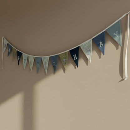 Handmade Birthday banner with blue and green flags made from baby clothing on a beige wall