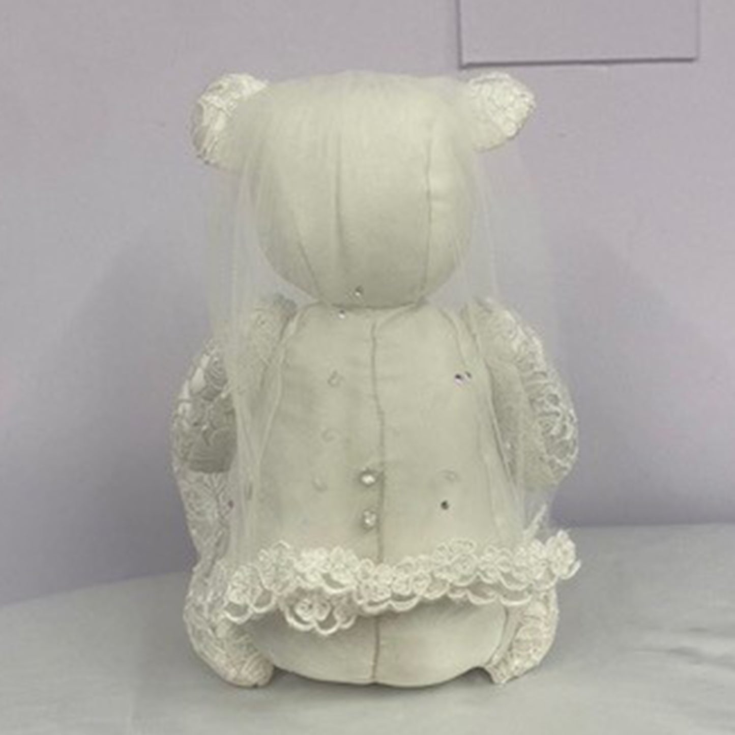 White teddy bear with a lace dress on a plain background