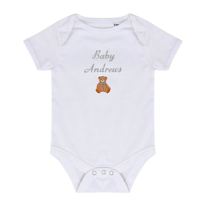 A white short-sleeve baby bodysuit with 'Baby Andrews' embroidered in gray script and a small brown teddy bear graphic on the chest, shown on a plain white background.