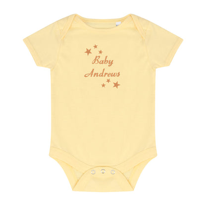 A pale yellow short-sleeve baby bodysuit with 'Baby Andrews' and small stars embroidered in a warm brownish-orange color on the chest, displayed flat against a white background.
