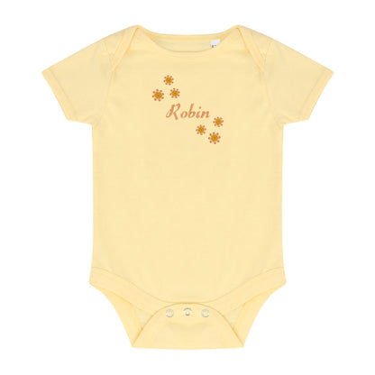 A pale yellow short-sleeve baby bodysuit with three snap buttons at the crotch and a custom graphic on the chest. The graphic features the name 'Robin' in a dusty rose script font, surrounded by small brown flower illustrations, set against a plain white background.