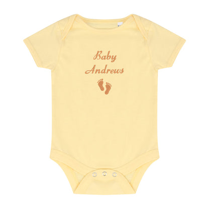 A pale yellow short-sleeve baby bodysuit with 'Baby Andrews' and baby footprints embroidered in brown on the chest, shown on a plain white background.