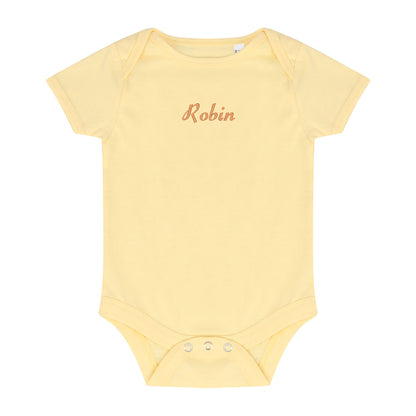 A pale yellow short-sleeve baby bodysuit with the name 'Robin' embroidered in a cursive peach font on the chest, displayed flat against a white background.
